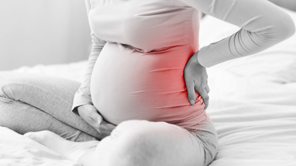 pregnant lady having backache sitting on bed in bedroom, cropped